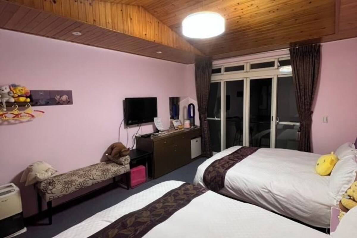Habitación de hotel con dos camas, un escritorio, un televisor de pantalla plana, un armario y una puerta corrediza de vidrio al exterior.