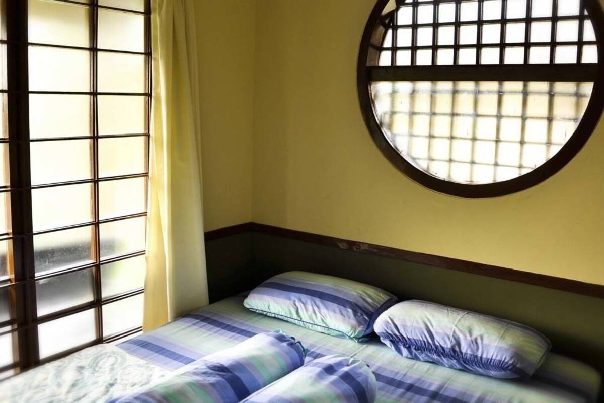 A room with a bed, a round window with a grid pattern, and a curtain.