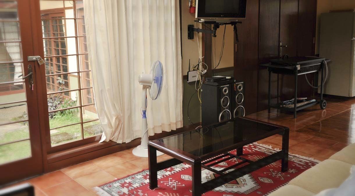 Un soggiorno con un tavolino in vetro, una TV su un mobile, una ventola e un carrello con dispositivi elettronici.