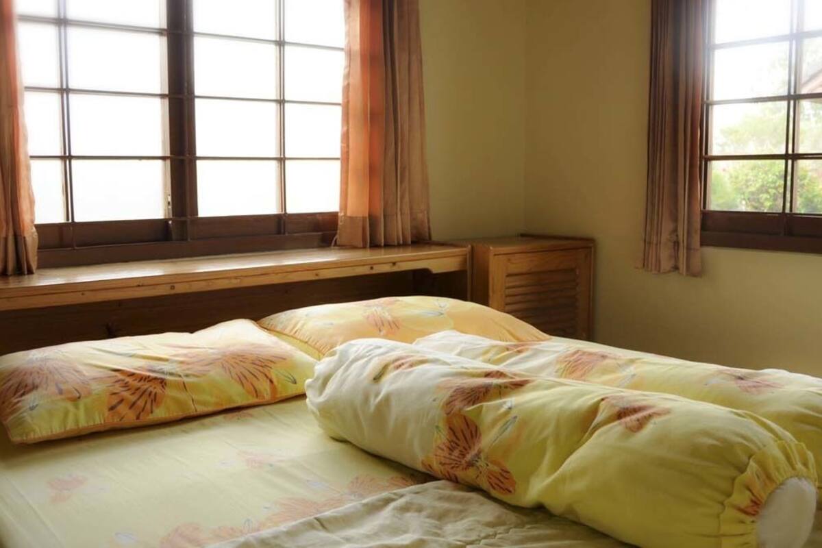A single bed with floral bedding, a wooden headboard, and a window with curtains.