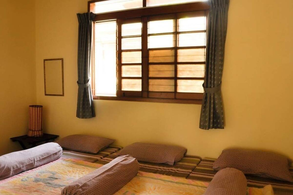A room with a bed, pillows, a nightstand, a window with curtains, and a wall-mounted mirror.