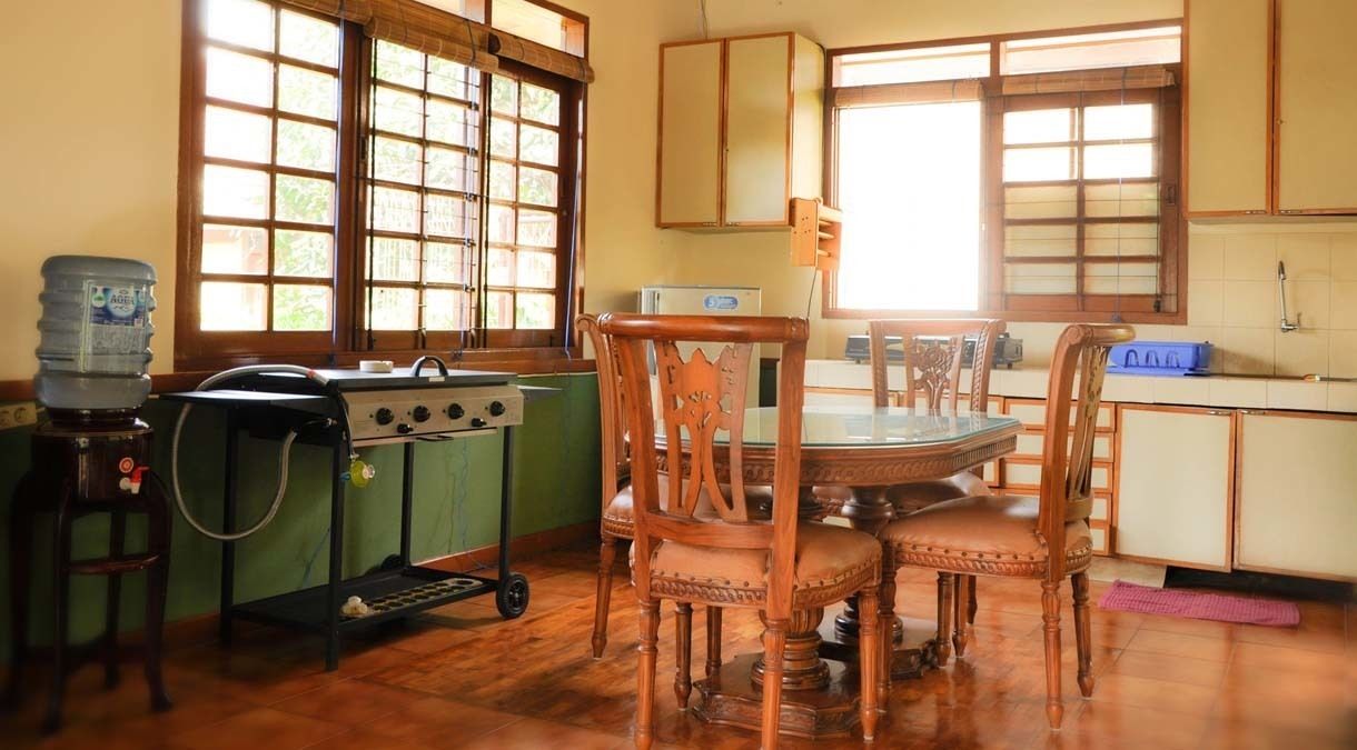 Una cocina con armarios de madera, estufa a gas, dispensador de agua y una mesa de comedor con sillas.