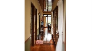 A hallway with wooden flooring, a tiled floor in the center, and a view of a dining area with a table and chairs. - Villa Kota Bunga Ade (Cipanas)