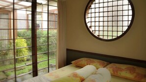 A room with a bed, a round window, and a view of greenery outside. - Villa Kota Bunga Ade (Cipanas)