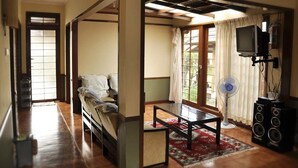 A traditional Japanese-style room with tatami flooring, a low table, a sofa, and a television. - Villa Kota Bunga Ade (Cipanas)