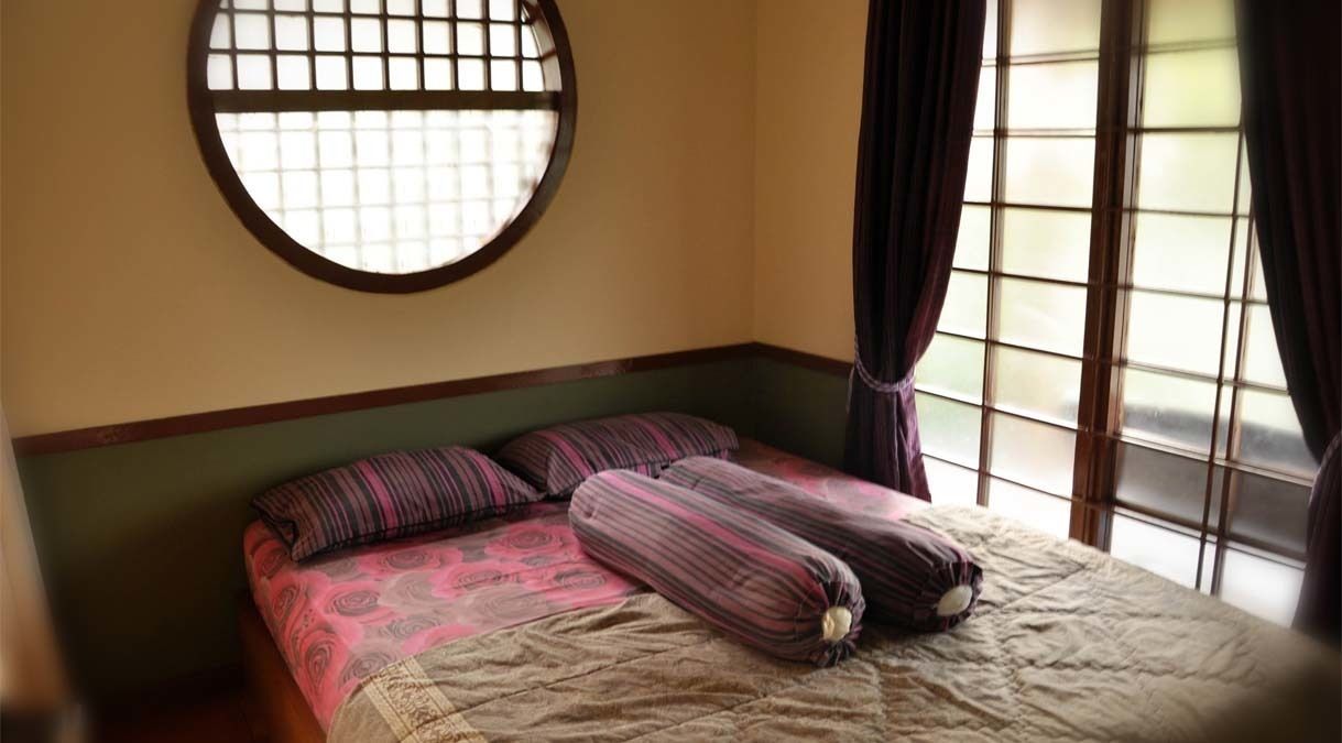 A room with a bed, a round window, and curtains.