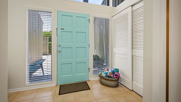 Une porte d’entrée de couleur bleu clair, un panier en métal contenant divers objets, et une vue sur l’extérieur.