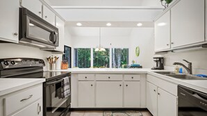 Une cuisine moderne avec des meubles blancs, une cuisinière noire, un four à micro-ondes et un lave-vaisselle.
