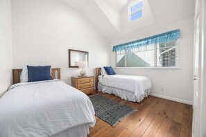 A bedroom with two beds, a dresser, a mirror, and a window with blinds.