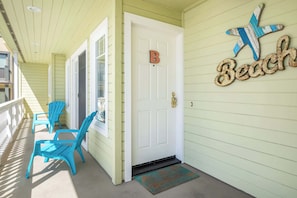 A porch with two blue Adirondack chairs, a white door with a 'B' sign, and a 'Beach' sign on the wall.