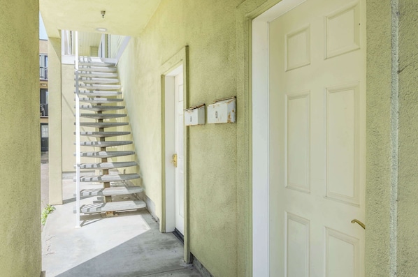A narrow hallway with a staircase leading to an upper floor, white doors, and a small window.