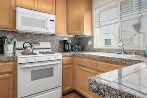 A kitchen with wooden cabinets, a white stove, a microwave, and granite countertops.
