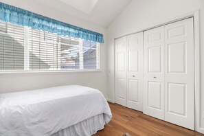 A bedroom with a bed, a window with blinds, and a set of white doors.