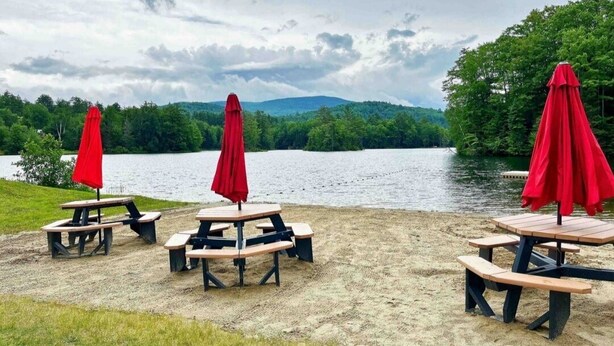 A lakeside picnic area with tables and red umbrellas.