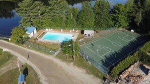 An aerial view of a property with a swimming pool, basketball court, and a road leading to the property.