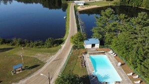 An aerial view of a property with a swimming pool, a small building, and a dock extending into a lake.