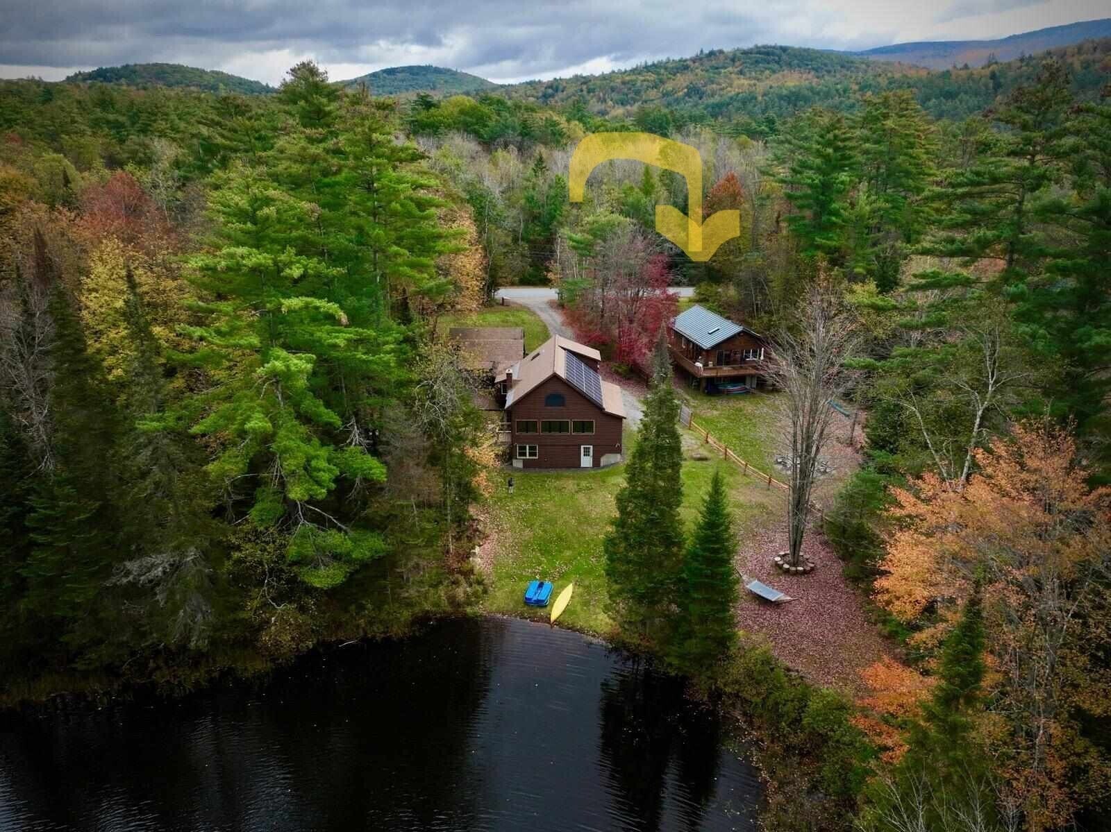 Une cabane dotée d’une grande fenêtre, entourée d’une forêt dense et bordée d’un lac.