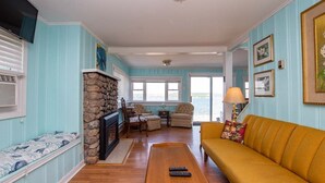 A living room with a stone fireplace, a yellow sofa, and a view of the water. - Deep Run Fun - Luxury Lake Life (Canandaigua)