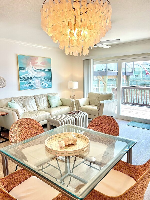 A modern living room with a glass coffee table, wicker chairs, a sofa, and a chandelier.