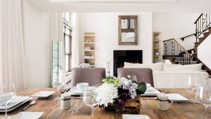 Un comedor con una mesa de madera dispuesta para una comida, una chimenea, una escalera y una estantería al fondo.