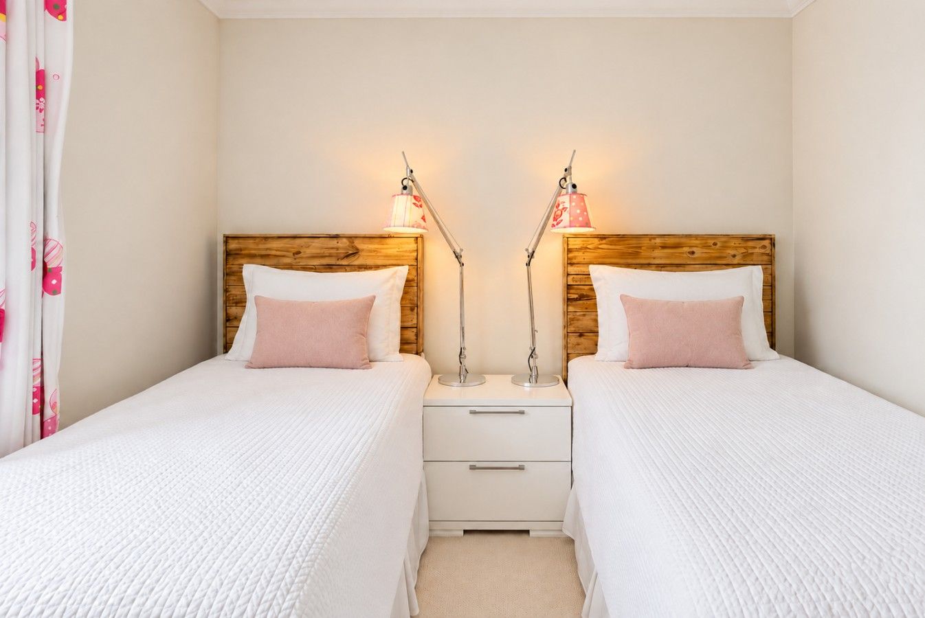 A twin room with two beds, each with a wooden headboard, white bedding, and bedside lamps. There is a small white nightstand with drawers between the beds.