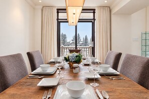 A dining table set for four with white plates, bowls, and cutlery, flanked by grey upholstered chairs.