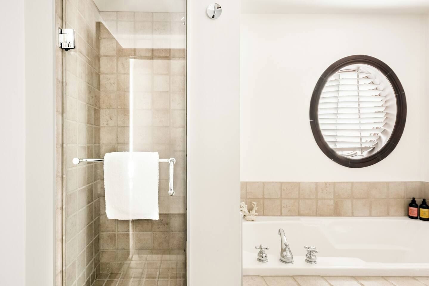 Ein Badezimmer mit einer Duschkabine aus Glas, einer weißen Badewanne und einem runden Fenster mit Jalousien.