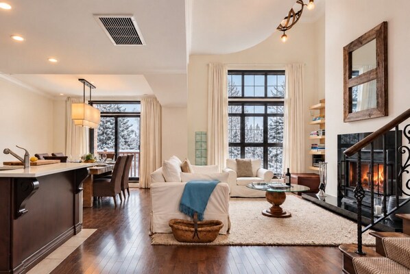 A spacious living area with a fireplace, a dining area with a view of snow-covered trees, and a kitchen with modern appliances.