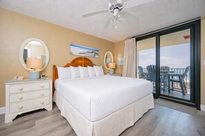 Une chambre d’hôtel avec un grand lit, deux tables de chevet, un ventilateur de plafond et une vue sur la plage, accessible par une porte-fenêtre coulissante.