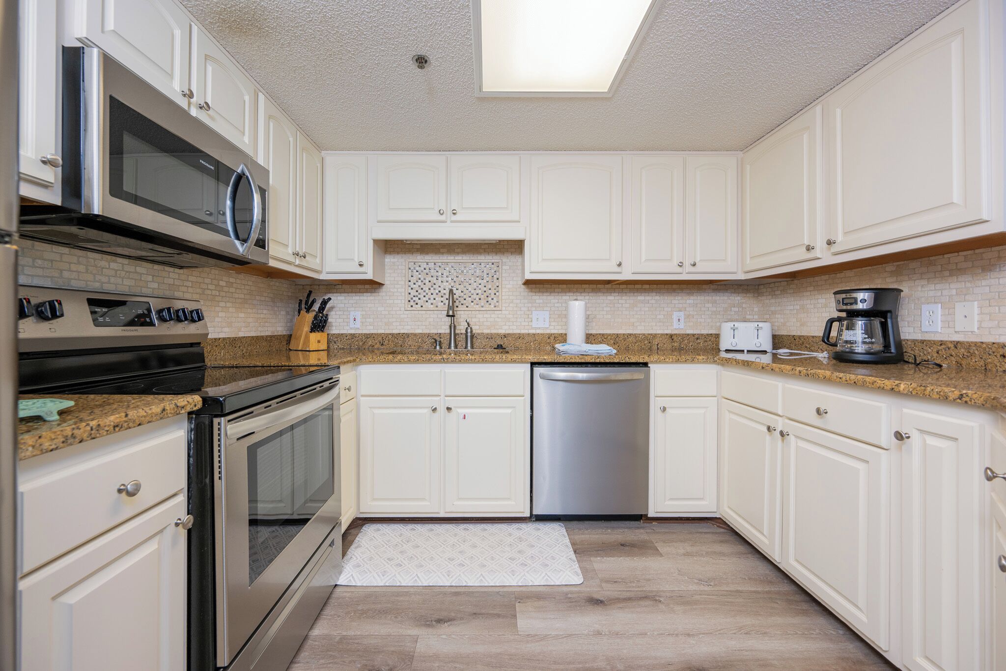 A kitchen with white cabinets, a stainless steel dishwasher, a microwave, and a coffee maker.