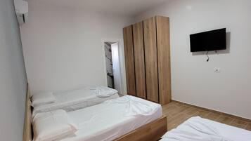 Ein Hotelzimmer mit zwei Einzelbetten, einem Holzschrank, einem an der Wand montierten Fernseher und einem kleinen Tisch mit Fernbedienung.