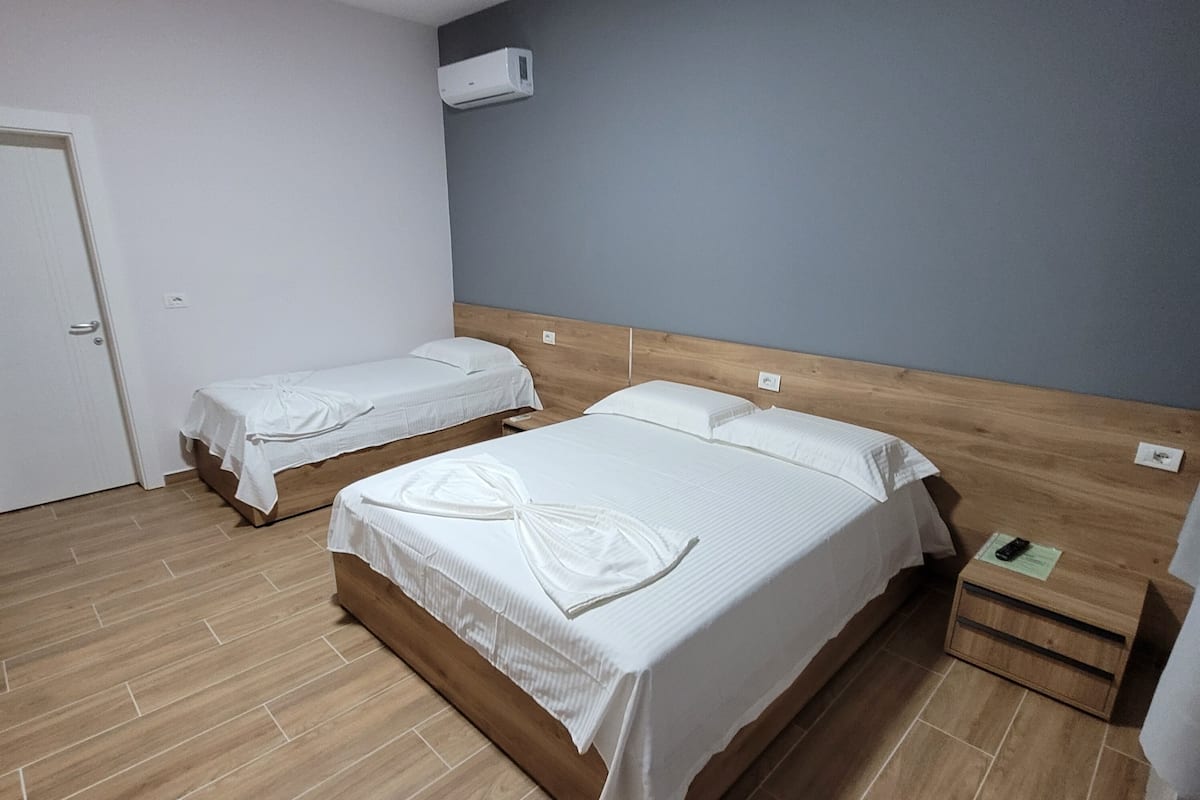 Habitación de hotel con dos camas, suelo de madera, una puerta blanca y un equipo de aire acondicionado en la pared.