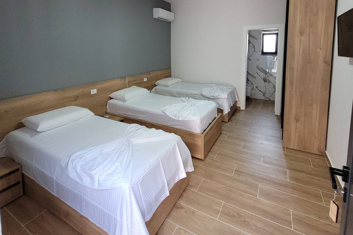 Una habitación de hotel con tres camas de madera, una pared gris y suelo de madera.