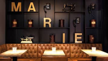 Un área de estar con una cabina y mesas, una pared con la palabra 'MARIE' escrita con letras, y teléfonos antiguos y recipientes.