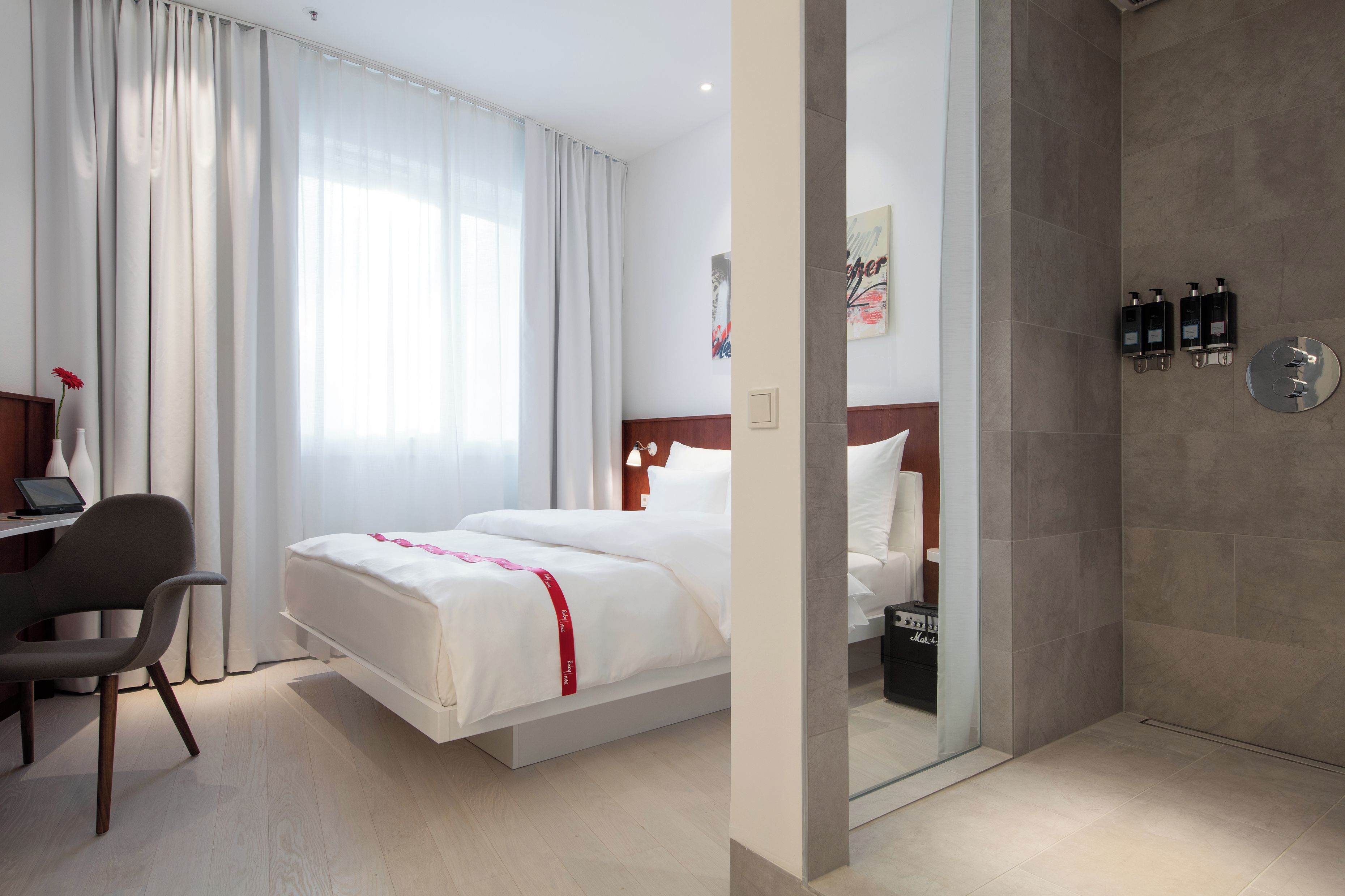 Habitación de hotel con cama, escritorio, silla y zona de ducha.