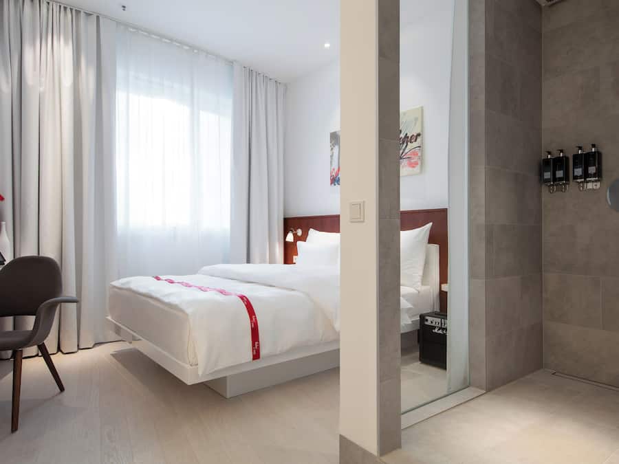 Habitación de hotel con cama, escritorio, silla y zona de ducha.