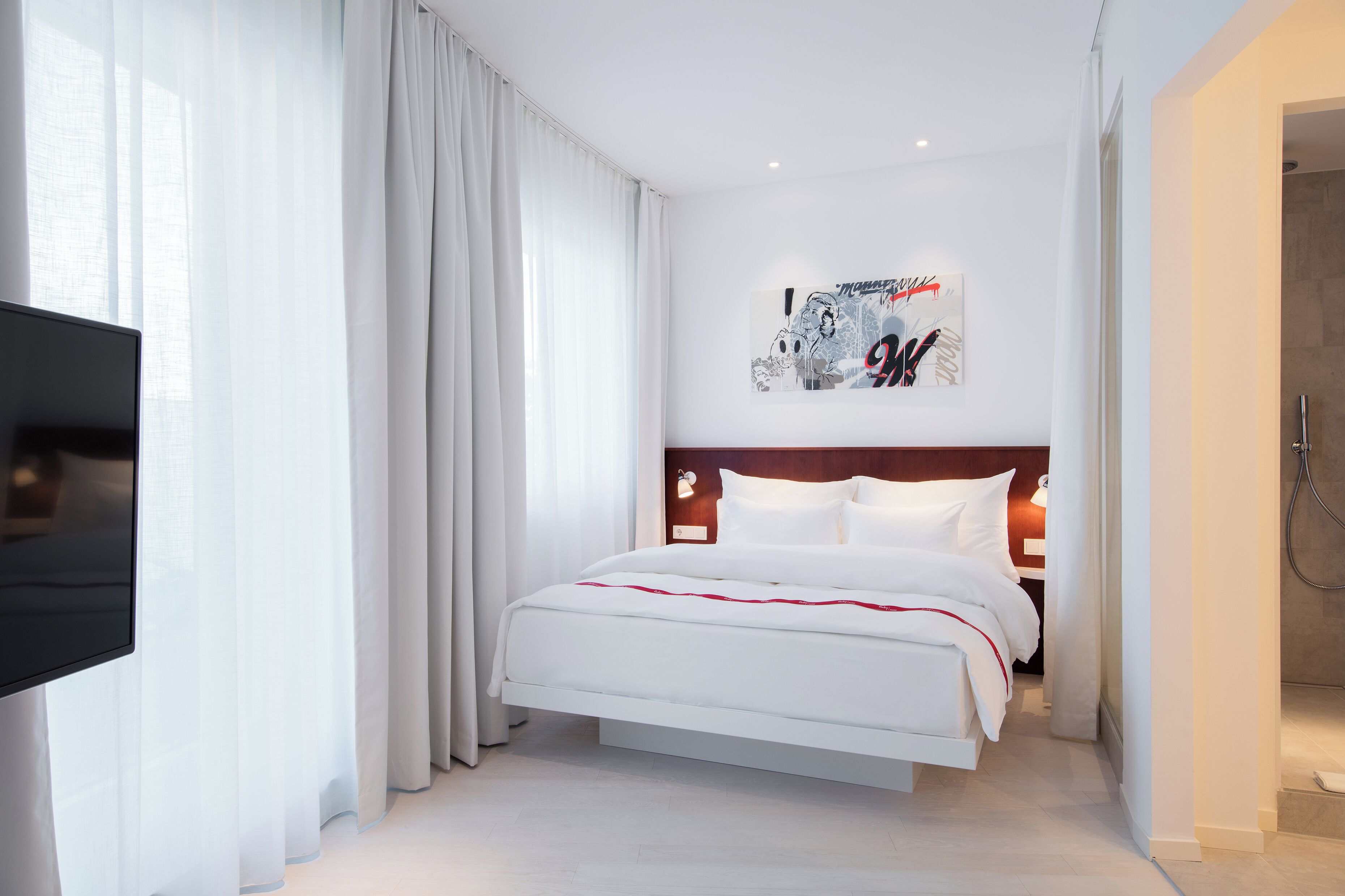 A modern hotel room with a large bed, a flat-screen TV, and a shower area.