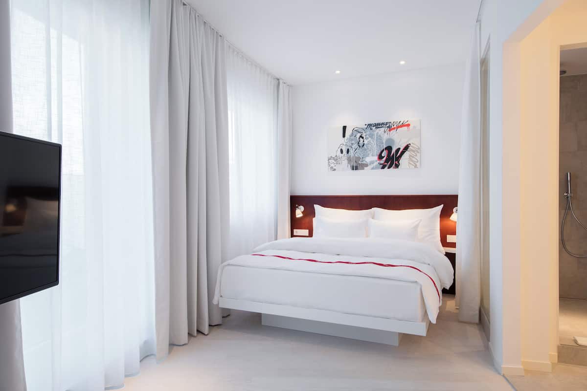 A modern hotel room with a large bed, a flat-screen TV, and a shower area.