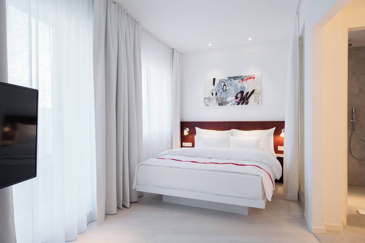 A modern hotel room with a large bed, a flat-screen TV, and a shower area.