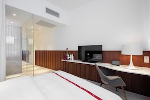 A modern hotel room with a bed, a desk with a television, a chair, and a bedside table with a lamp. - Ruby Marie Hotel Vienna by IHG (Vienna)