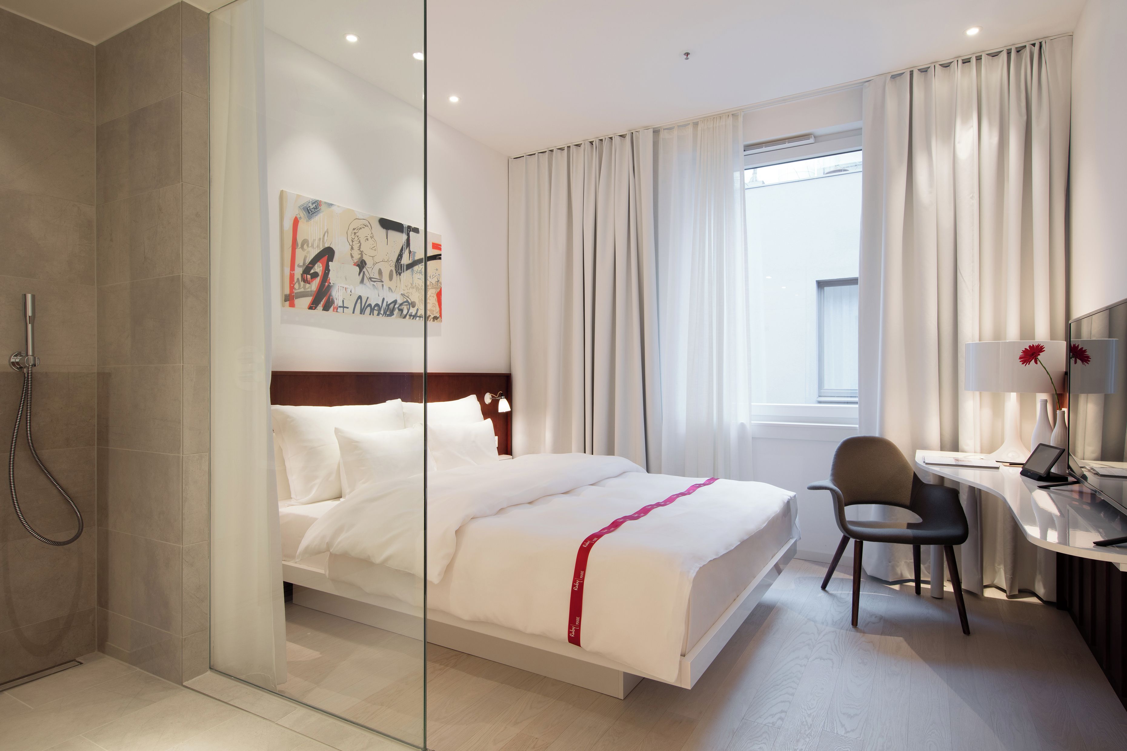 Une chambre d’hôtel moderne équipée d’un lit, d’un bureau, d’une chaise et d’un espace douche.