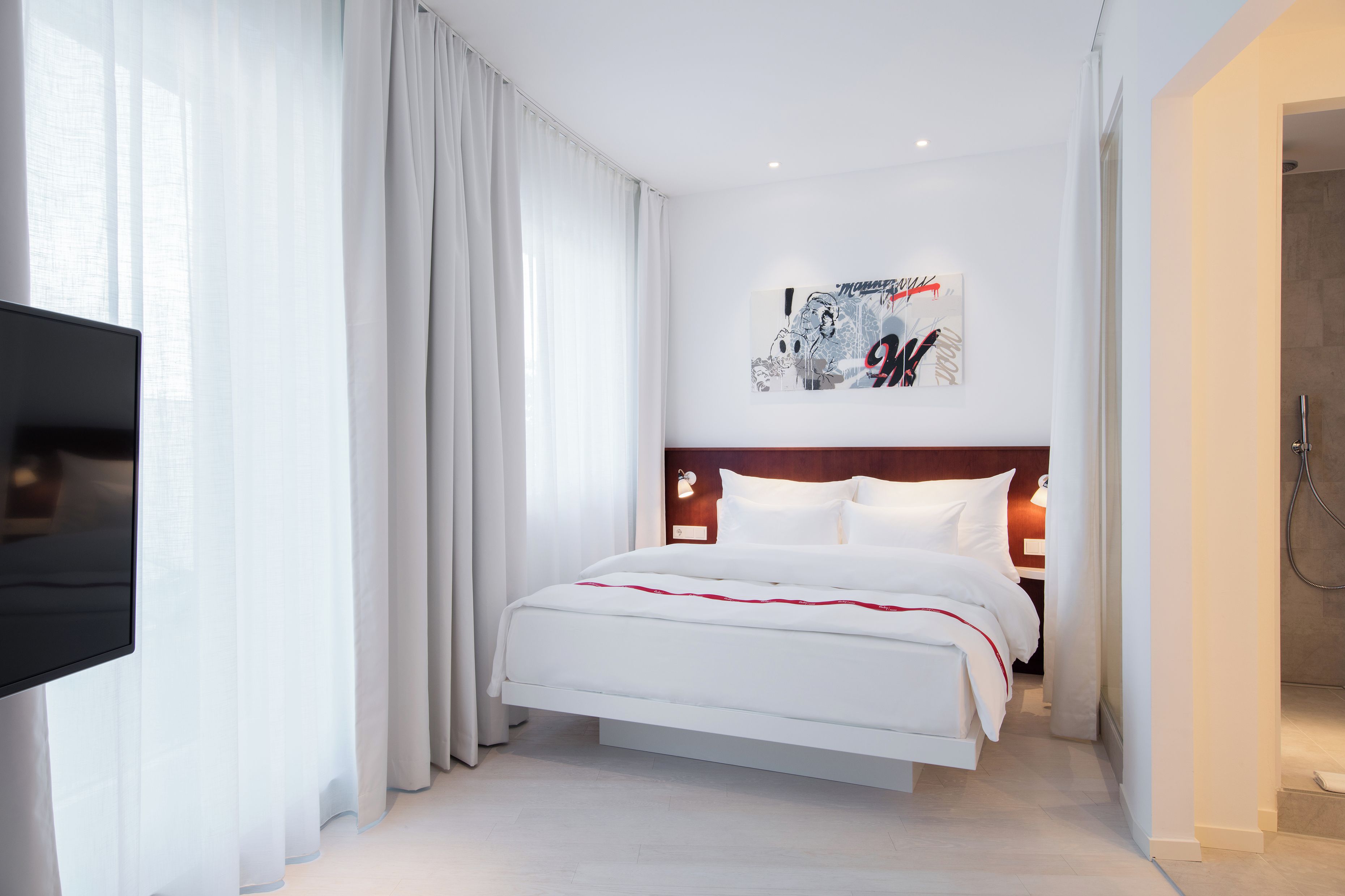 Una habitación de hotel moderna con una cama grande, un televisor de pantalla plana y una zona de ducha.