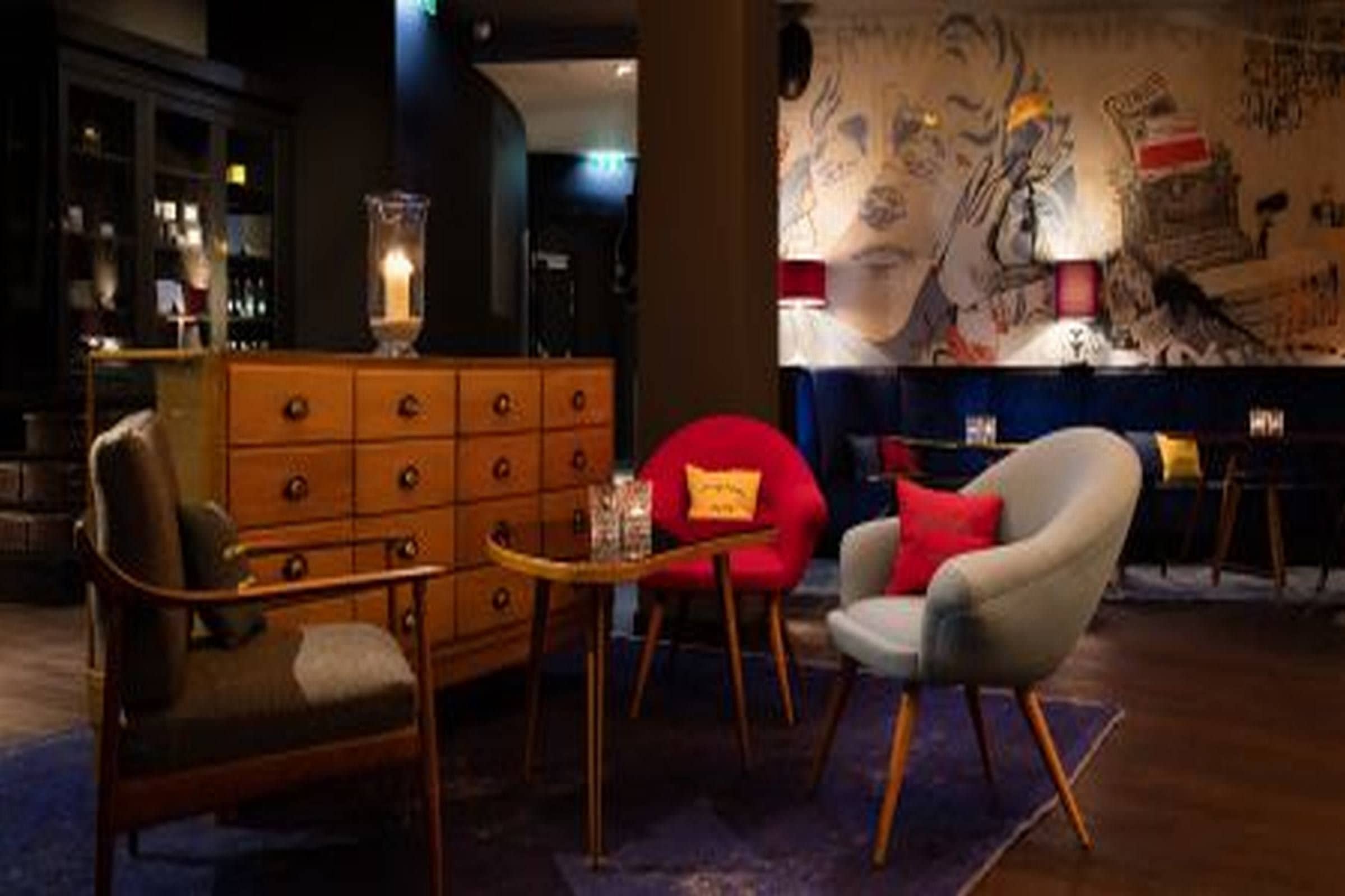 Una habitación con un aparador de madera, dos sillones, una mesita y una pared con arte abstracto.