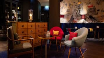 Una habitación con un aparador de madera, dos sillones, una mesita y una pared con arte abstracto.