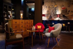 Una habitación con un aparador de madera, dos sillones, una mesita y una pared con arte abstracto.