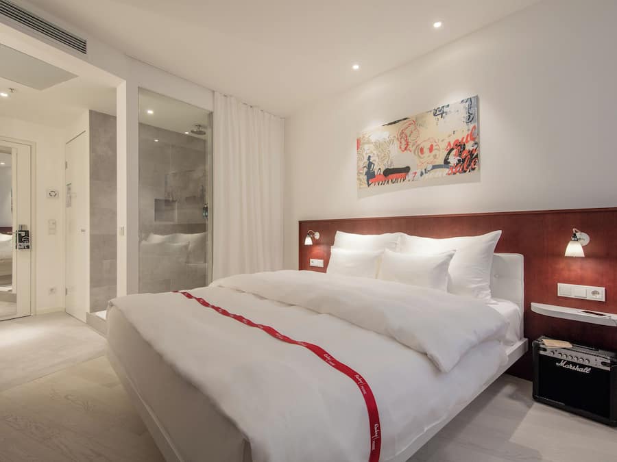 Une chambre d’hôtel avec un grand lit, une douche, un tableau au mur et une petite table avec une lampe.