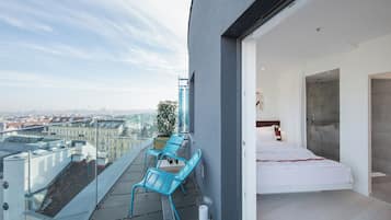 Un balcón moderno con cama y ducha, con vistas a un paisaje urbano.