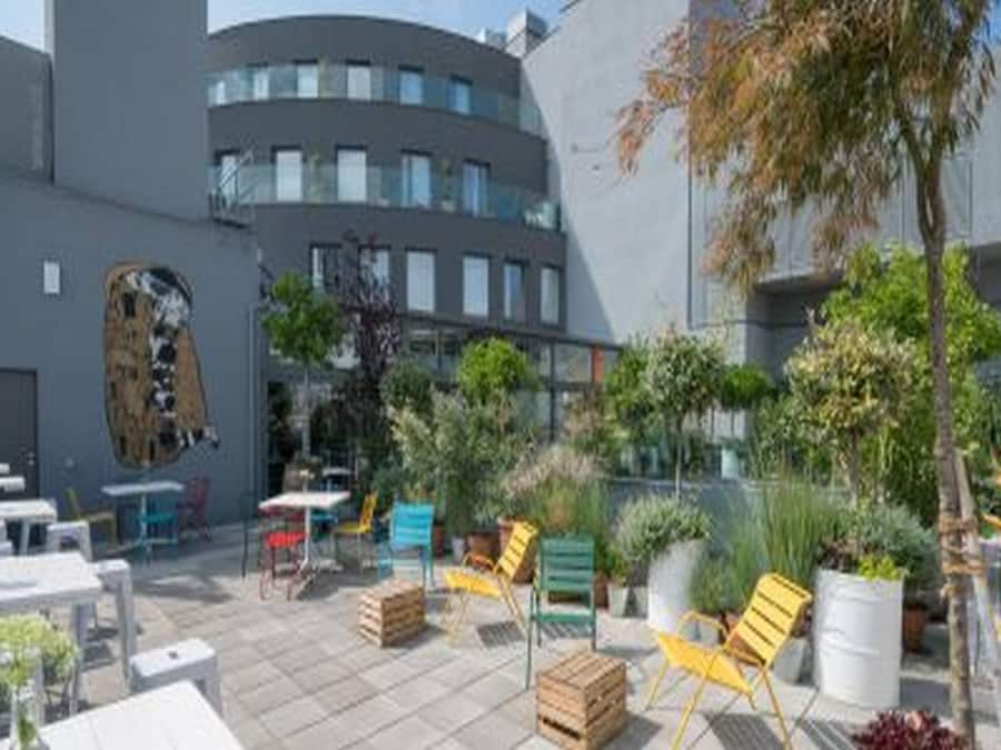 An outdoor patio area with tables and chairs, surrounded by buildings.
