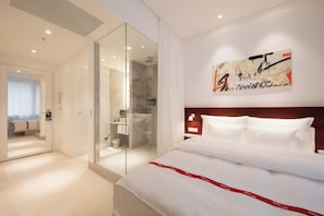 A hotel room with a large bed, a glass-enclosed shower, and a wall-mounted artwork. - Ruby Marie Hotel Vienna by IHG (Vienna)