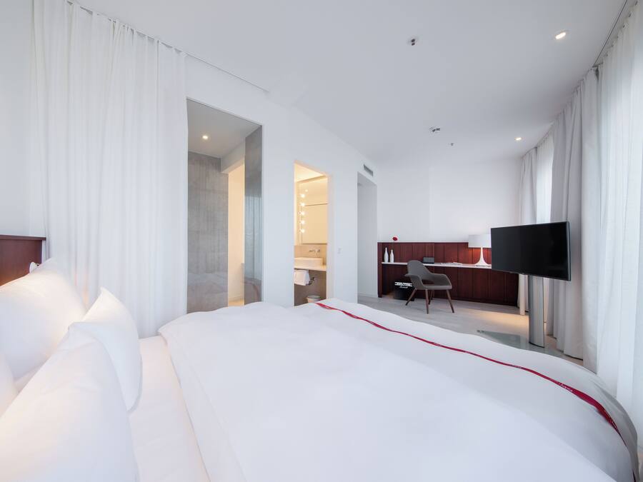 A modern hotel room with a large bed, a desk, and a TV.